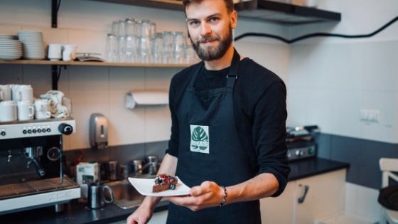 man wearing barista apron holding dessert