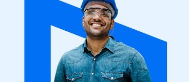 smiling tradesman wearing a hardhat and holding a tablet.