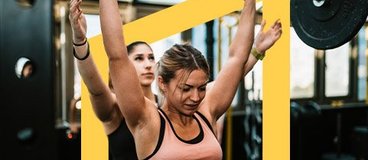 Woman in pink tank top lifting weight with woman in black spotting behind her.