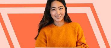 girl in orange sweatshirt with laptop on peach background.