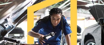 Auto mechanic in blue jumpsuit inspecting car engine.
