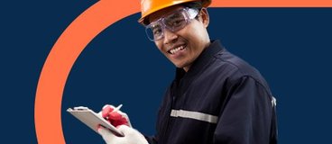 Man in orange hard hat and safety goggles making notes on clipboard.