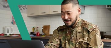Man wearing Army fatigues using laptop in kitchen.