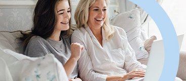Mom and daughter sitting on couch using white laptop.