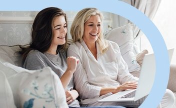 Mom and daughter sitting on couch using white laptop.