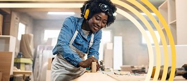 Woman in denim shirt and apron doing woodwork.