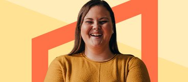 Girl in yellow sweater smiling in front of orange background.