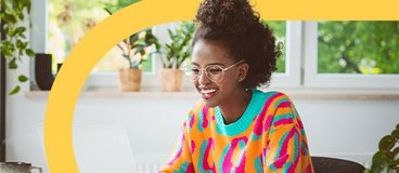 Girl in bright sweater studying with pile of books and laptop.