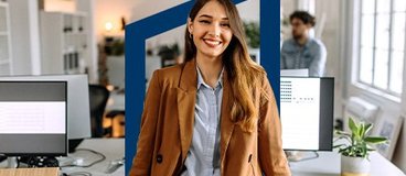 Smiling woman in office wearing brown coat.