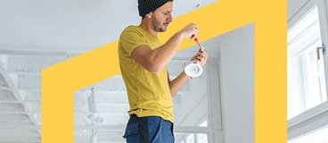 Man in yellow shirt fixing light fixture.