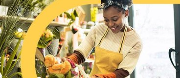 Woman in yellow apron arranging flowers.