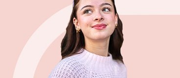girl with brown hair in white sweater on light red background.