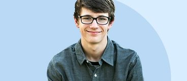 Boy in button up shirt and glasses smiling.