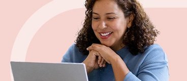 Woman in blue looking at silver laptop smiling.