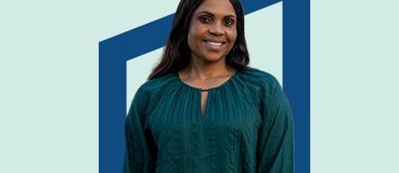 Woman in dark green blouse in front of blue background.