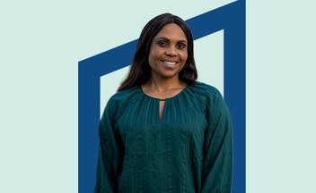 Woman in dark green blouse in front of blue background.