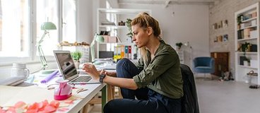 A person sits on a chair in a creative studio, light filled studio, working on a computer