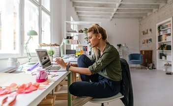 A person sits on a chair in a creative studio, light filled studio, working on a computer