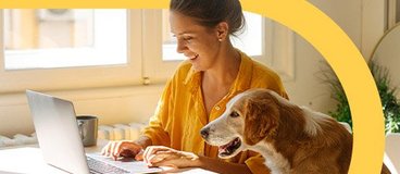 Woman in yellow shirt using laptop with dog beside her.