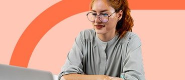 woman with red hair and glasses writing notes from a laptop.