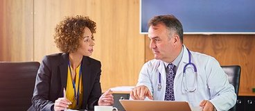 Two people sit in a boardroom, discussing something on a computer screen