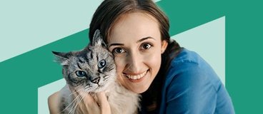 Vet tech in blue scrubs holding gray tabby cat on green background.