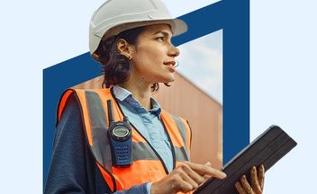 Woman in orange safety vest and white hard hat using tablet.