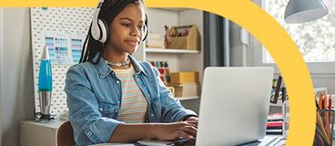 Girl wearing denim jacket in headphones using laptop.