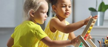 Two preschool-age children, both wearing yellow, playing with a toy