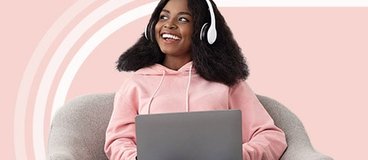 Girl in pink hoodie with headphones using laptop.