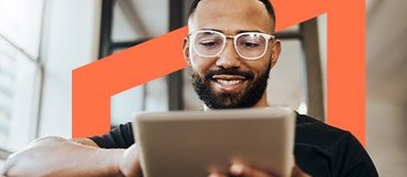 Man wearing glasses sitting on couch and scrolling on tablet.