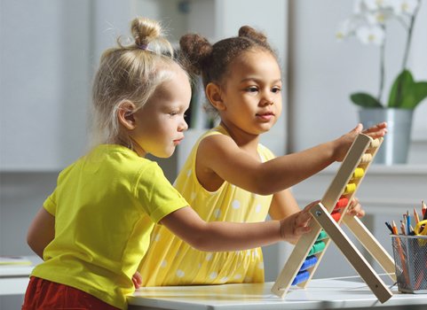 Two preschool-age children, both wearing yellow, playing with a toy
