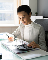 A person with dark skin and dark hair wears a suit and uses a calculator 