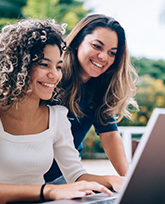 Two woman look at a computer screen, smiling 