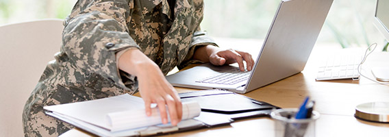 person in military uniform on a computer sitting at a desk.