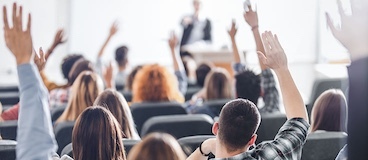 people sitting in an auditorium with their hands raised.