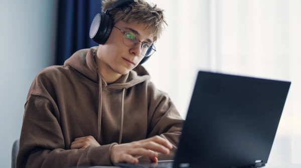 Teen boy in hoodie and headphones using laptop.
