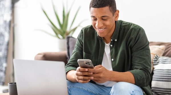 Teen boy smiling at cell phone in front of laptop.