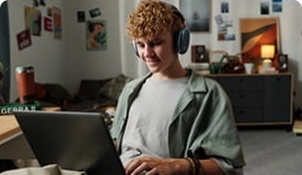 Teen boy in green shirt wearing headphones studying on laptop.