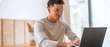 Young man in light colored shirt with sleeves pushed up typing on laptop.