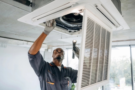 HVAC technician examining air duct with flashlight.