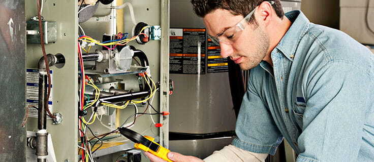 HVAC technician wearing safety glasses working on open HVAC system.