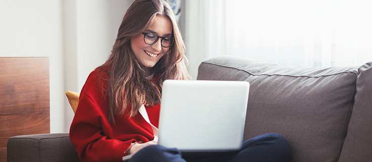 woman seated on a couch on the computer smiling.