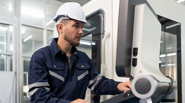 man in white hardhat operating CNC machine.