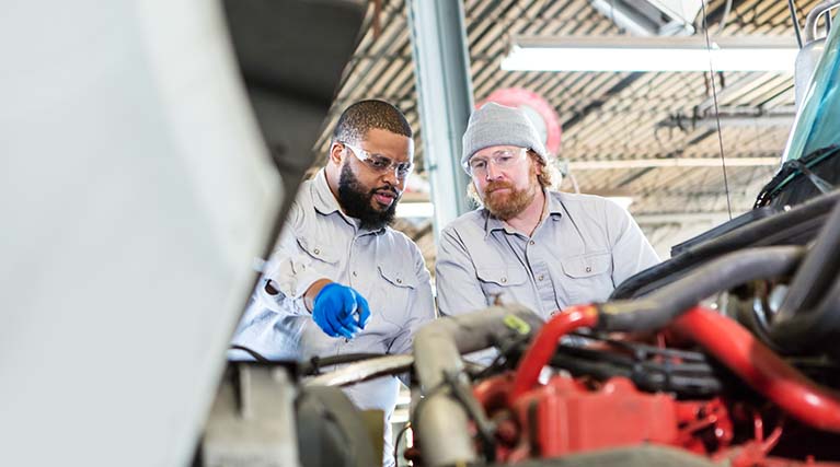 two mechanics inspect diesel truck engine.