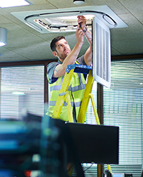 Maintenance worker fixing ceiling light in office.