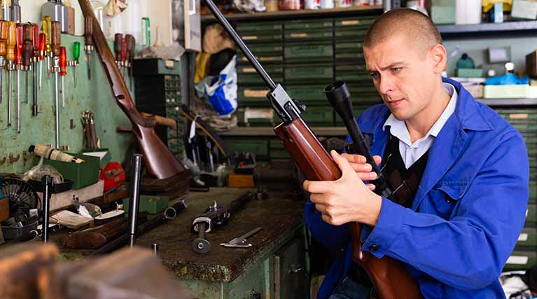 gunsmith inspects rifle scope in workshop.