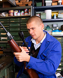 gunsmith inspects rifle scope in workshop.