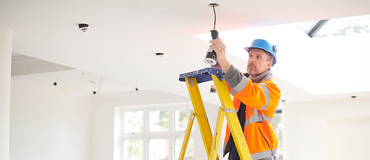 electrician on ladder installing lights in home.