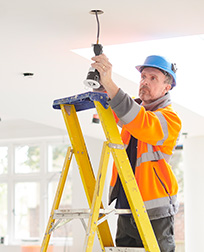 electrician on ladder installing lights in home.